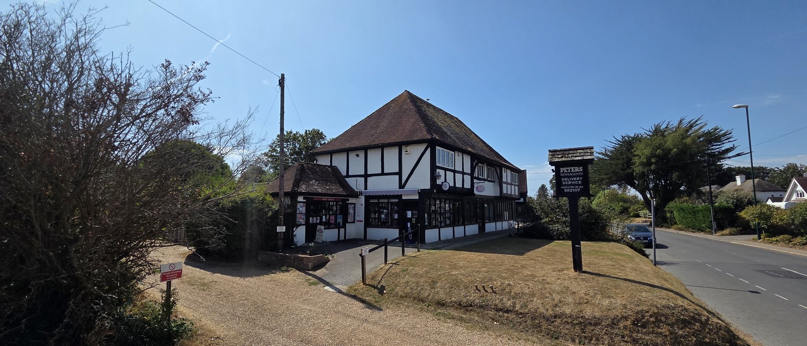 Peters Newsagents, a black and white mock-Tudor building on a corner with a post office sign on the smaller wing beside it, and a tall sign by the road reading Peters Newsagents Delivery Service