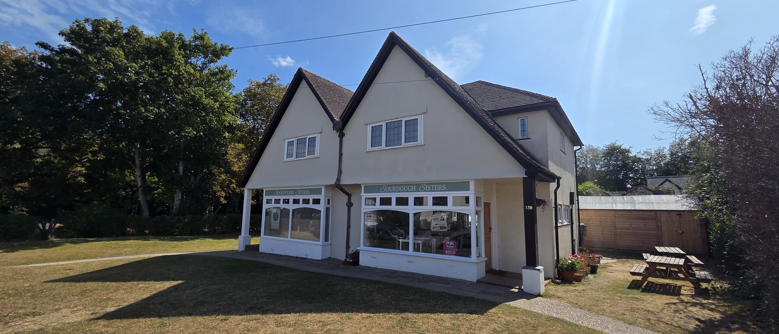 A pair of gabled shopfronts signed Sourdough Sisters, with white framed windows and a green grass verge in front