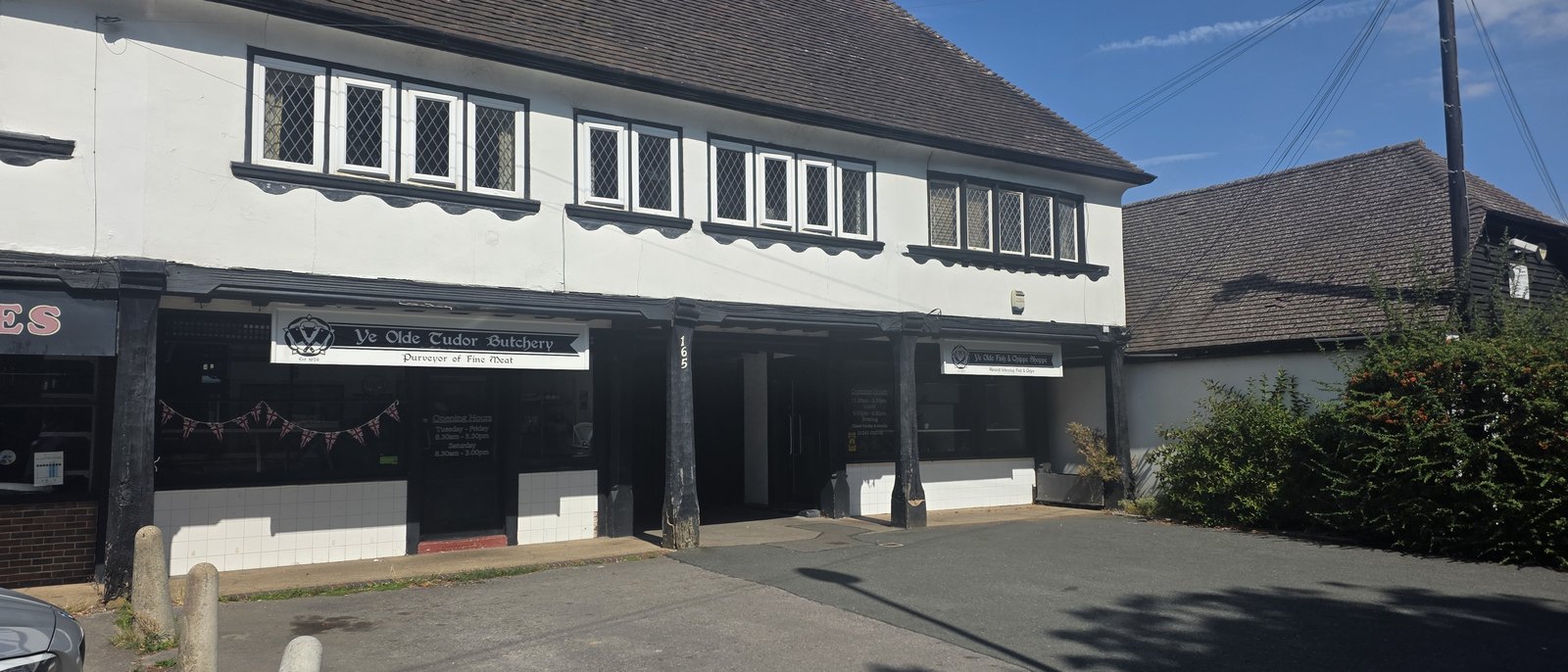 A white and black mock-Tudor parade with leaded windows above and two shopfronts below, one signed Ye Olde Tudor Butchery, Purveyor of Fine Meat, the other Ye Olde Fish and Chipps Shoppe